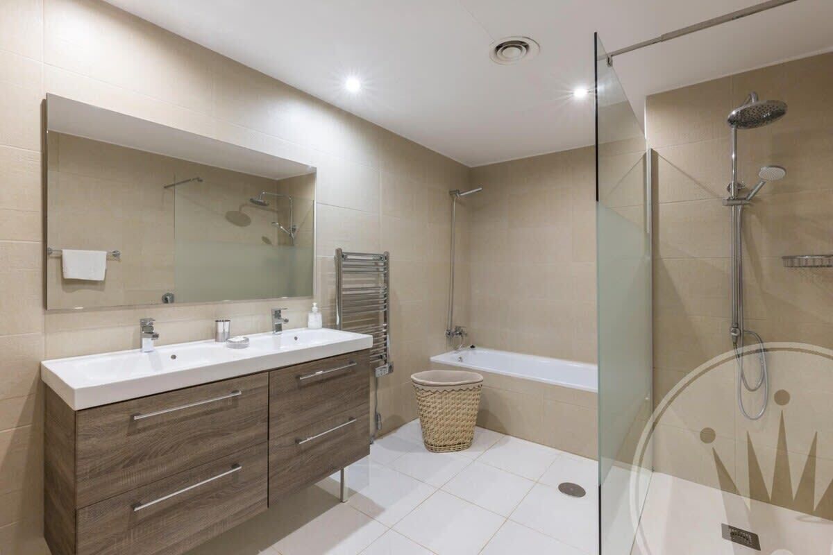 Une salle de bain moderne dotée d’une douche à parois de verre, d’un grand miroir et d’un meuble-lavabo à deux vasques.