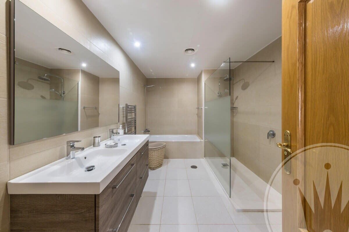 Une salle de bain moderne dotée d’un grand miroir, d’un meuble-lavabo à deux vasques, d’une baignoire et d’une cabine de douche en verre.
