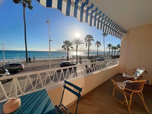 A balcony with a view of the beach, palm trees, and cars on the road.