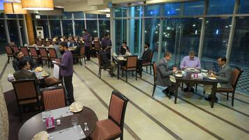 A spacious dining area with multiple tables and chairs, large windows offering a view of the outdoors, and a modern interior design.