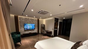 A modern hotel room with a large bed, a television, a seating area, and a bathroom. - Jacaranda Heights (Islamabad)