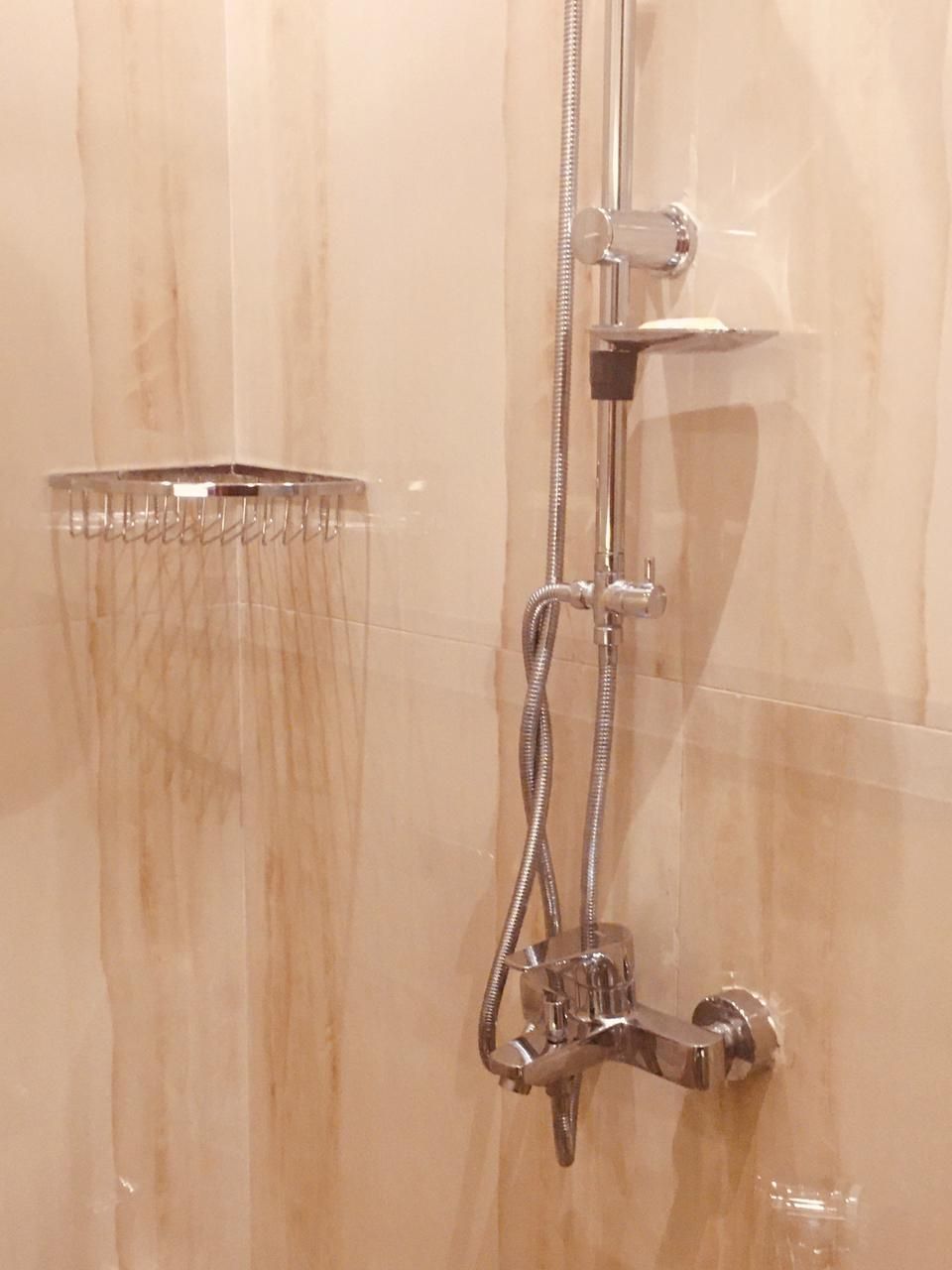 Ducha con manguera de mano y cabezal de ducha empotrado en un baño con paredes de azulejos color beige.