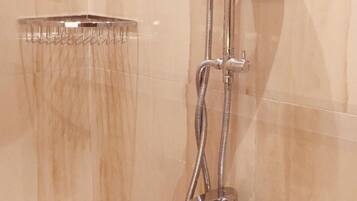 Ducha con manguera de mano y cabezal de ducha empotrado en un baño con paredes de azulejos color beige.