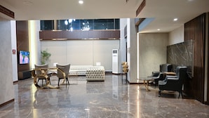 A spacious lobby with a marble floor, a seating area with a sofa and chairs, and a television screen. - Jacaranda Heights (Islamabad)