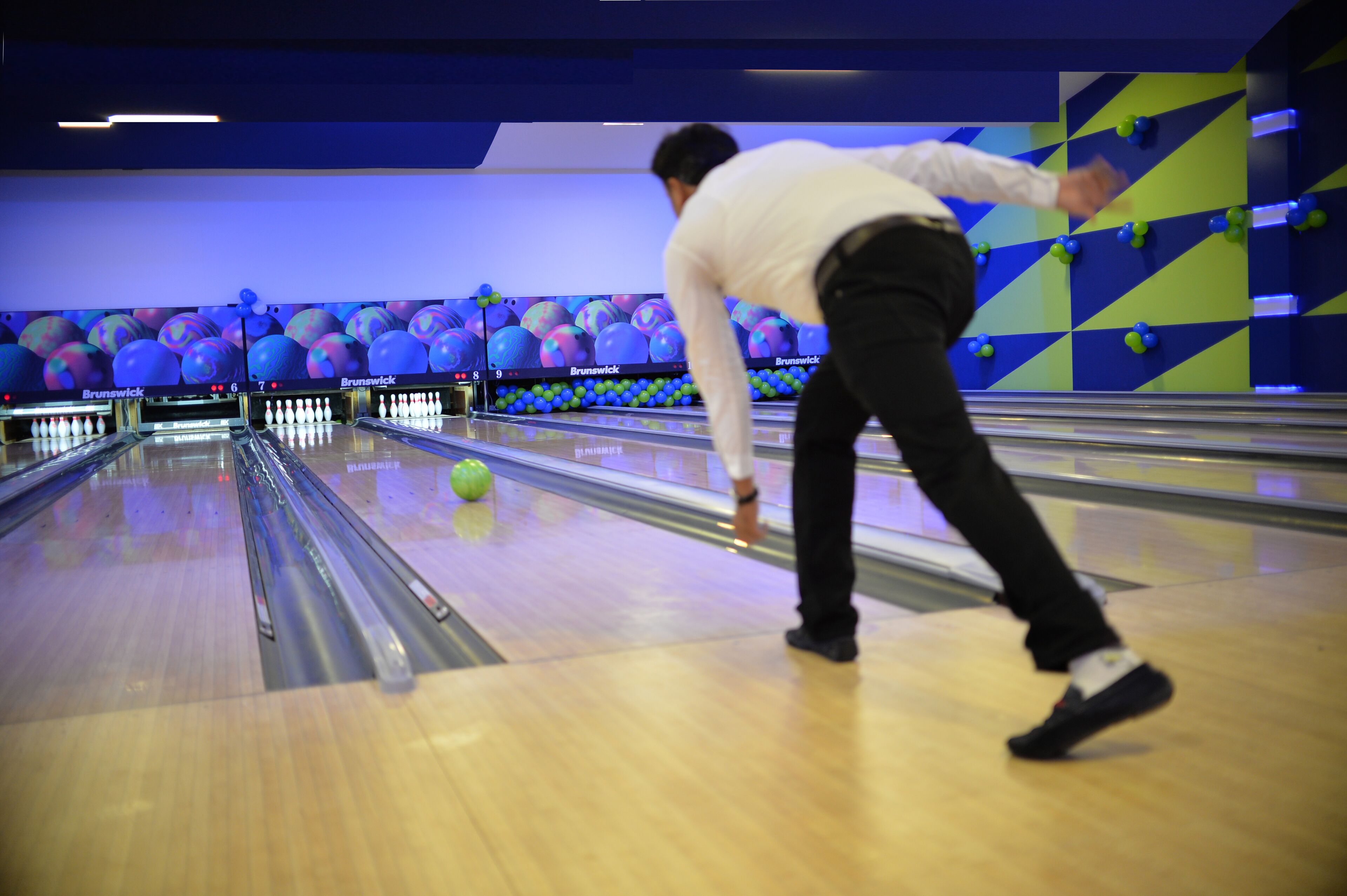 A bowling alley with multiple lanes and a person in a white shirt bowling.