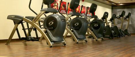 A row of stationary bikes in a gym with wooden flooring and motivational posters on the wall.
