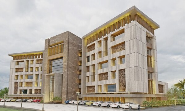 A modern hotel with a symmetrical facade, multiple balconies, and a parking lot with several cars.