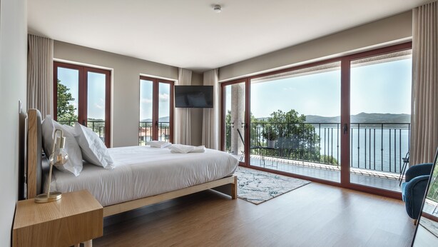 Een moderne slaapkamer met een groot bed, een aan de muur bevestigde televisie en een balkon met uitzicht op het water.