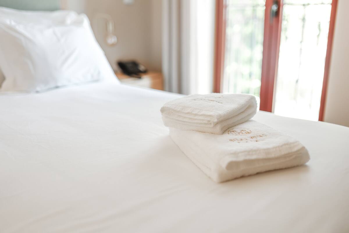 A neatly made bed with folded white towels and a visible phone on the nightstand.