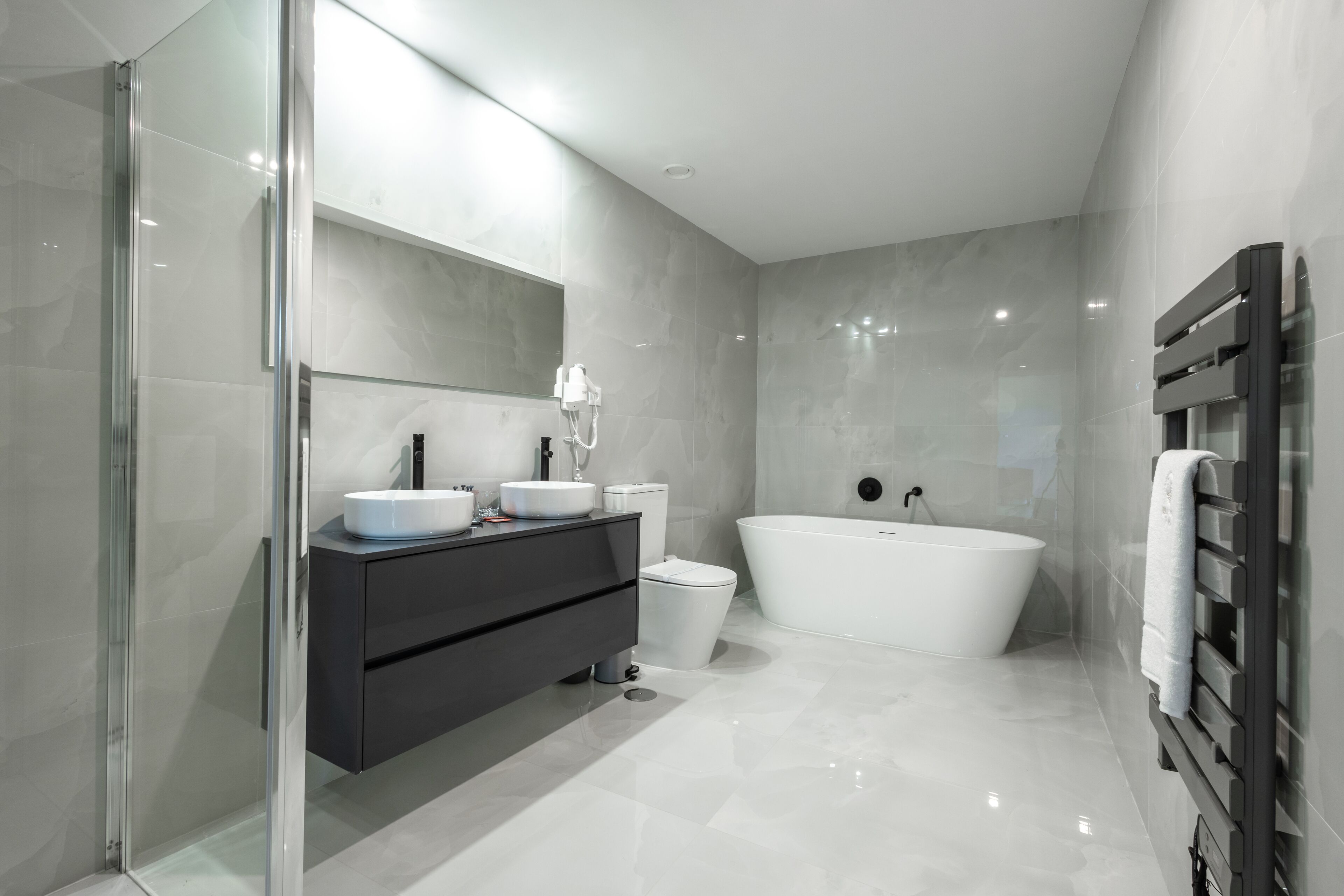 Une salle de bain moderne dotée d’une douche à parois de verre, d’une baignoire sur pieds, d’un meuble-lavabo foncé avec un miroir et d’un porte-serviettes.