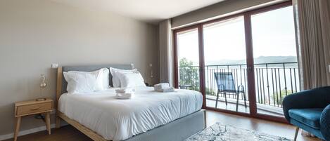 Ein modernes Hotelzimmer mit einem großen Bett, einem Nachttisch, einem Sessel und einem Balkon mit Blick.