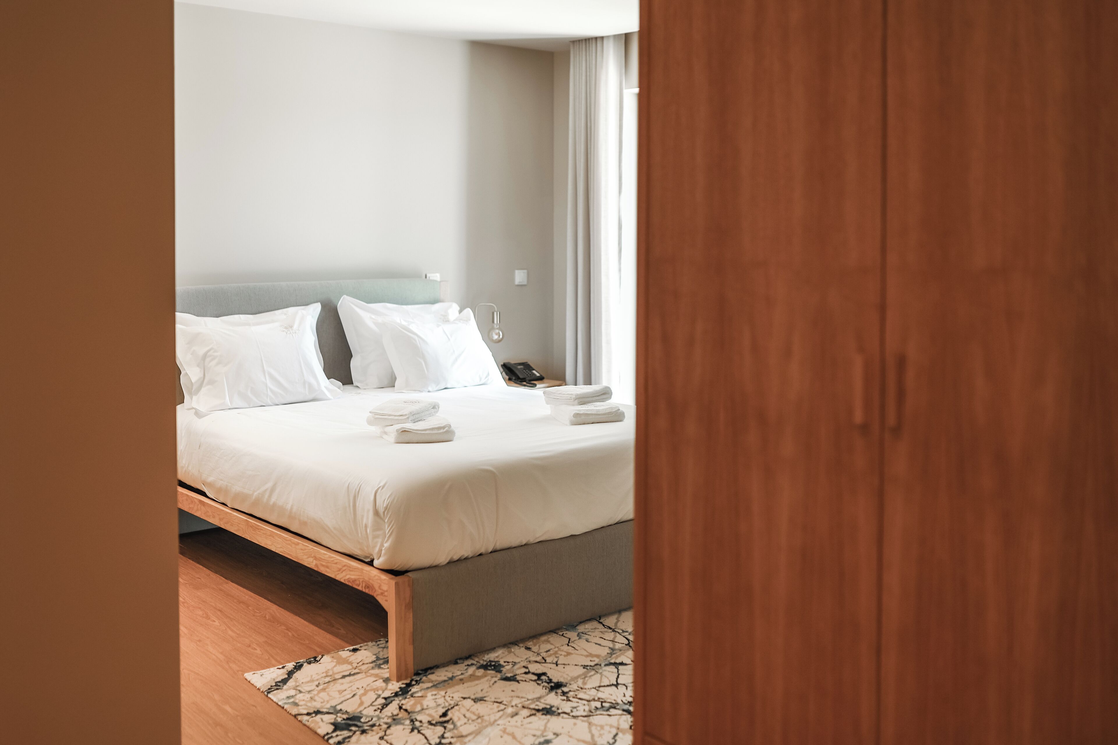 Una camera da letto moderna con una struttura letto in legno, biancheria da letto bianca e un tappeto con motivo marmorizzato.