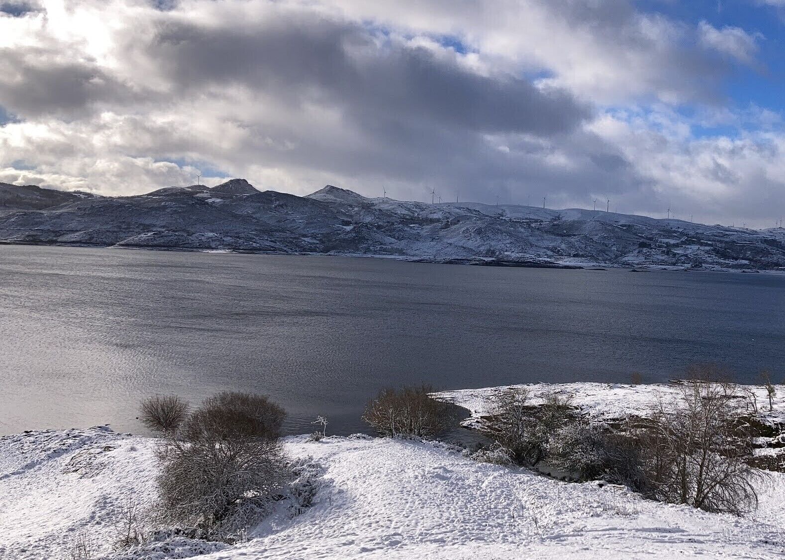 A snowy landscape with a frozen lake and mountains in the background.