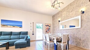 A living room with a sofa, dining table with chairs, a chandelier, and a beach painting. - Casa Kody - with BBQ, Fiber optic, private parking and silence.  (La Oliva)
