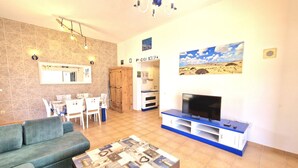 A living room with a sofa, a coffee table, a TV, and a dining area with a table and chairs. - Casa Kody - with BBQ, Fiber optic, private parking and silence.  (La Oliva)