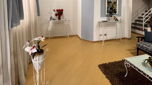 Un salon avec un plancher en bois, une table blanche ornée d’un vase de fleurs, une console blanche, un tableau accroché au mur et un escalier en arrière-plan.