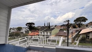 Un balcon doté d’un sol carrelé et offrant une vue sur un quartier résidentiel avec des maisons et des arbres.