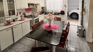 Une cuisine avec des meubles blancs, une table à manger noire surmontée d’un set de table rose, et une voiture blanche garée à l’extérieur.