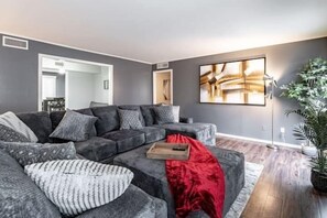 A modern living room with a grey sectional sofa, a red throw blanket, and a large abstract painting on the wall. - Hoff Gardens 9 - 2BR 2BA - Downtown Lubbock (Lubbock)