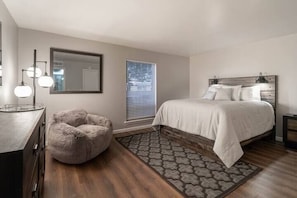 Un dormitorio con cama, cómoda, silla, espejo y ventana con persianas.