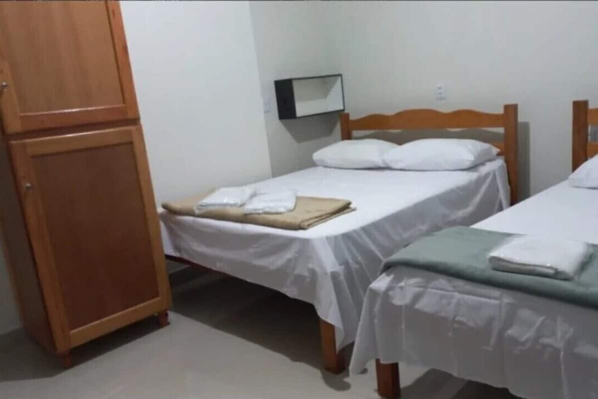Ein Zimmer mit zwei Einzelbetten, Holz-Kopfteilen, weißer Bettwäsche, einem Holzschrank und einem kleinen Nachttisch mit Lampe.
