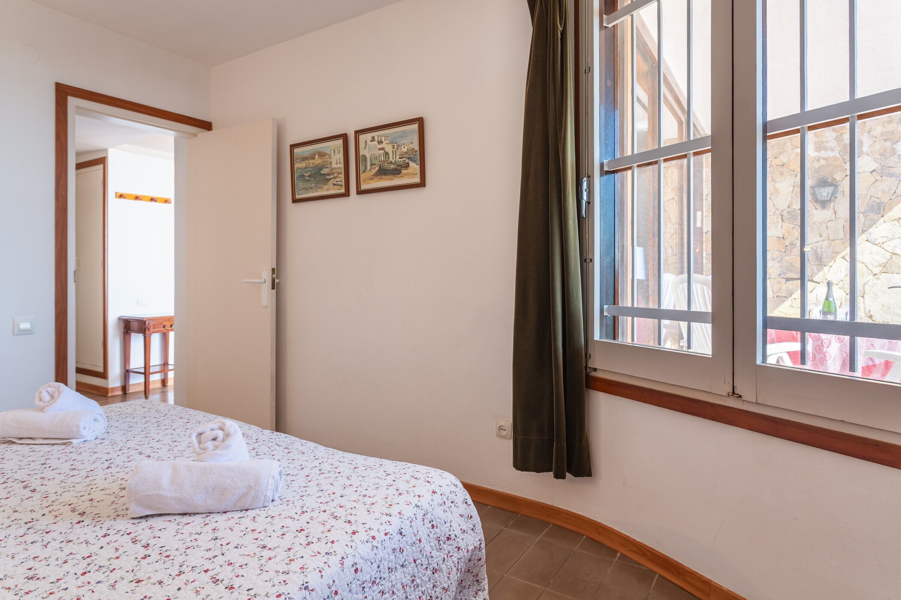Ein Hotelzimmer mit einem Bett, zwei gerahmten Bildern an der Wand, einem Fenster mit Vorhängen und Blick nach draußen.