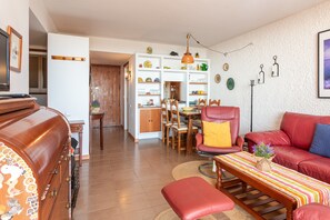 Un salon avec un canapé rouge, une table basse en bois et un coin repas comprenant une table et des chaises en bois.
