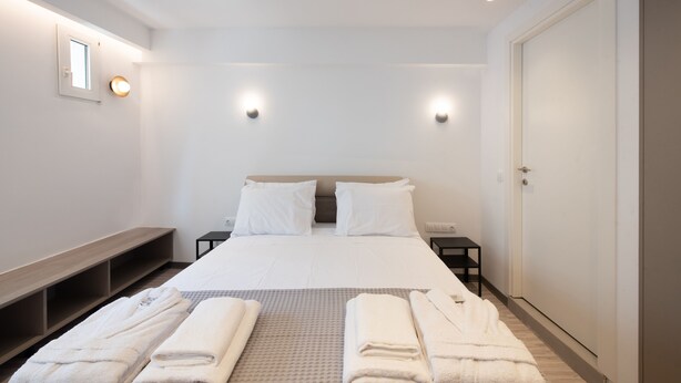 Ein modernes Hotelzimmer mit einem großen Bett, Nachttischen, einer Bank und einem Kleiderschrank.