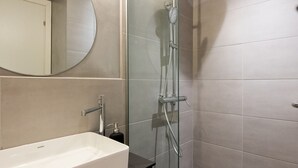 Ein modernes Badezimmer mit Duschkabine aus Glas, einem weißen Waschbecken und einem großen Spiegel.