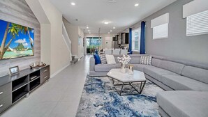 A modern living room with a grey sofa, a coffee table, and a TV mounted on the wall. - 5 En-Suites | Close to Disney! (Davenport)
