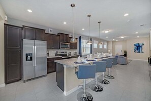 A modern kitchen with dark cabinets, stainless steel appliances, a central island with bar stools, pendant lighting, and a large abstract painting on the wall.