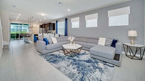 A modern living room with a grey sofa, a coffee table, and a view of the kitchen. - 5 En-Suites | Close to Disney! (Davenport)