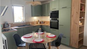 A compact kitchen with a dining area, featuring a built-in oven, a coffee machine, and a wooden bookshelf. - Cancoon - Holiday Apartment Rental Cancale (Cancale)