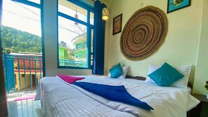 Habitación de hotel con una cama, un ventanal grande, un adorno en la pared y vista a un edificio verde en el exterior.