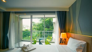 Ein Hotelzimmer mit einem großen Bett, einem Fenster mit Vorhängen und Blick auf Grün sowie einem Tisch mit Stühlen.