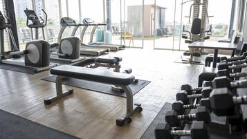 A gym with exercise equipment, a bench, and dumbbells.