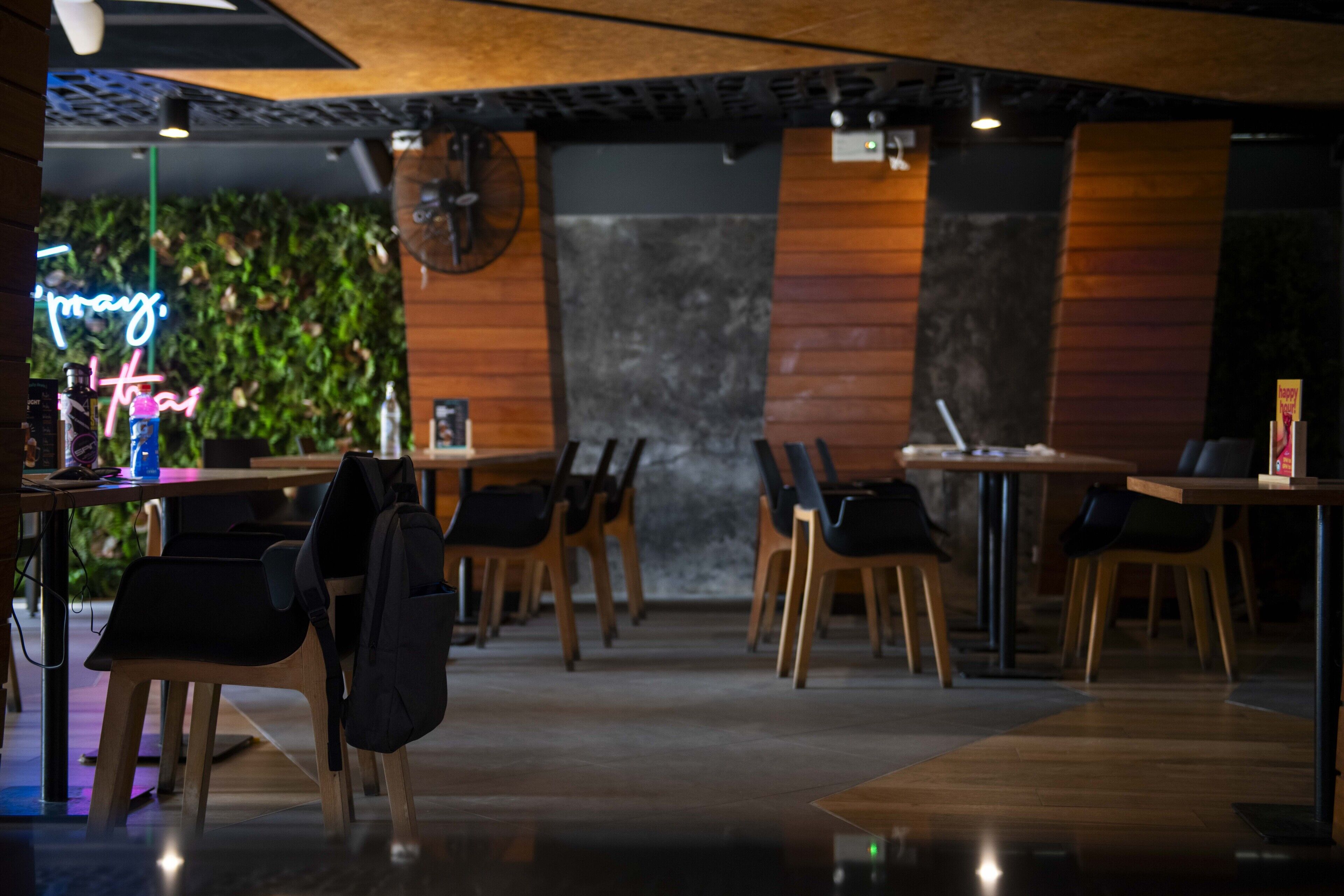A modern restaurant interior with wooden tables and chairs, a neon sign, and a wall-mounted fan.