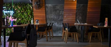 A modern restaurant interior with wooden tables and chairs, a neon sign, and a wall-mounted fan.