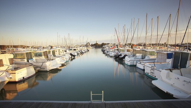 A marina with multiple boats docked in calm water, a wooden dock in the foreground, and a clear sky. - Le Secret des Marées (Givrand)