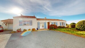A two-story house with a tiled roof, a driveway, and a garden with various plants and flowers. - Le Secret des Marées (Givrand)