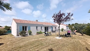 A single-story house with a tiled roof, a small patio with outdoor furniture, and a tree in the yard. - Le Secret des Marées (Givrand)