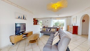 A modern living room with a grey sofa, a wooden TV stand, and a dining area with a table and chairs. - Le Secret des Marées (Givrand)