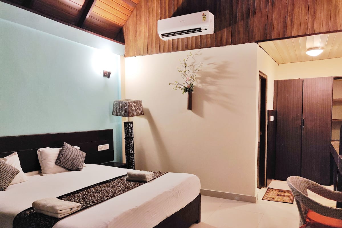 Un dormitorio con cama, lámpara de noche, aire acondicionado y una planta pequeña en la pared.