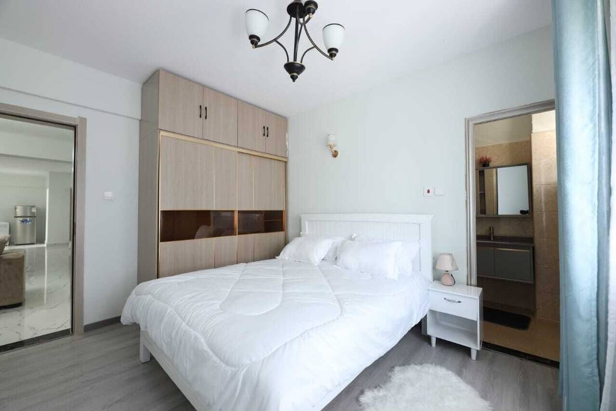 A modern bedroom with a large bed, a wardrobe, a bedside table, and a mirror.