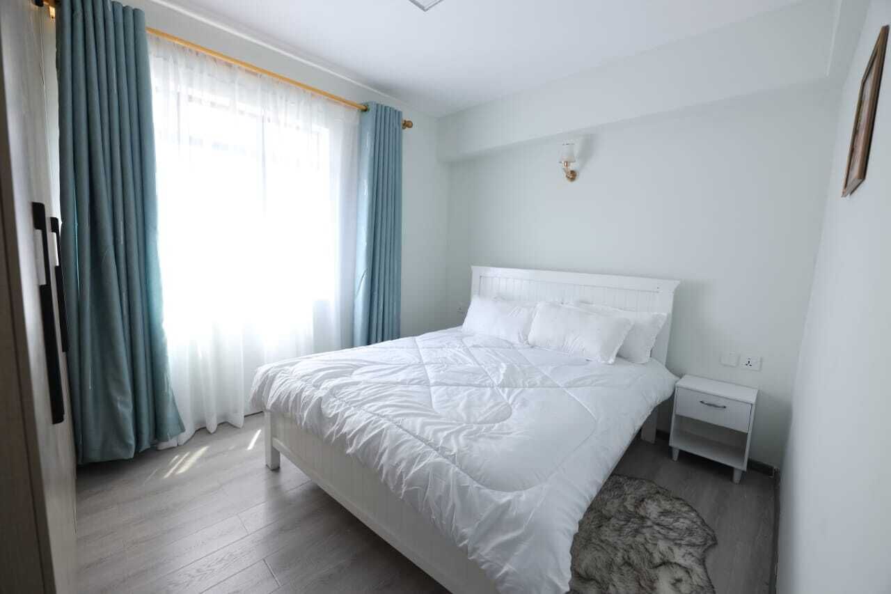 Une chambre à coucher comprenant un lit, une table de chevet, une lampe fixée au mur et une fenêtre avec des rideaux.