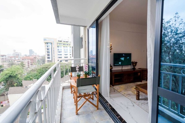 A balcony with a dining table and chairs, a television, and a view of the cityscape. - Lux Suites Sandalwood Gardens Apartments (Nairobi)
