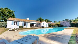 Une maison avec une piscine, une terrasse dotée de chaises longues et un petit jardin.
