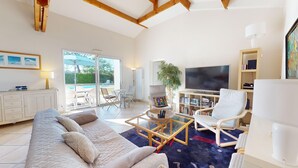 Un salon spacieux avec un grand canapé, une table basse et un téléviseur. Une porte-fenêtre coulissante donne accès à un espace extérieur avec une piscine.