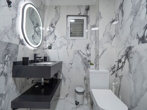 A modern bathroom with a marble backsplash, a round mirror, a toilet, and a sink with a black countertop. - Apartments Cataleya Przno (Pržno)
