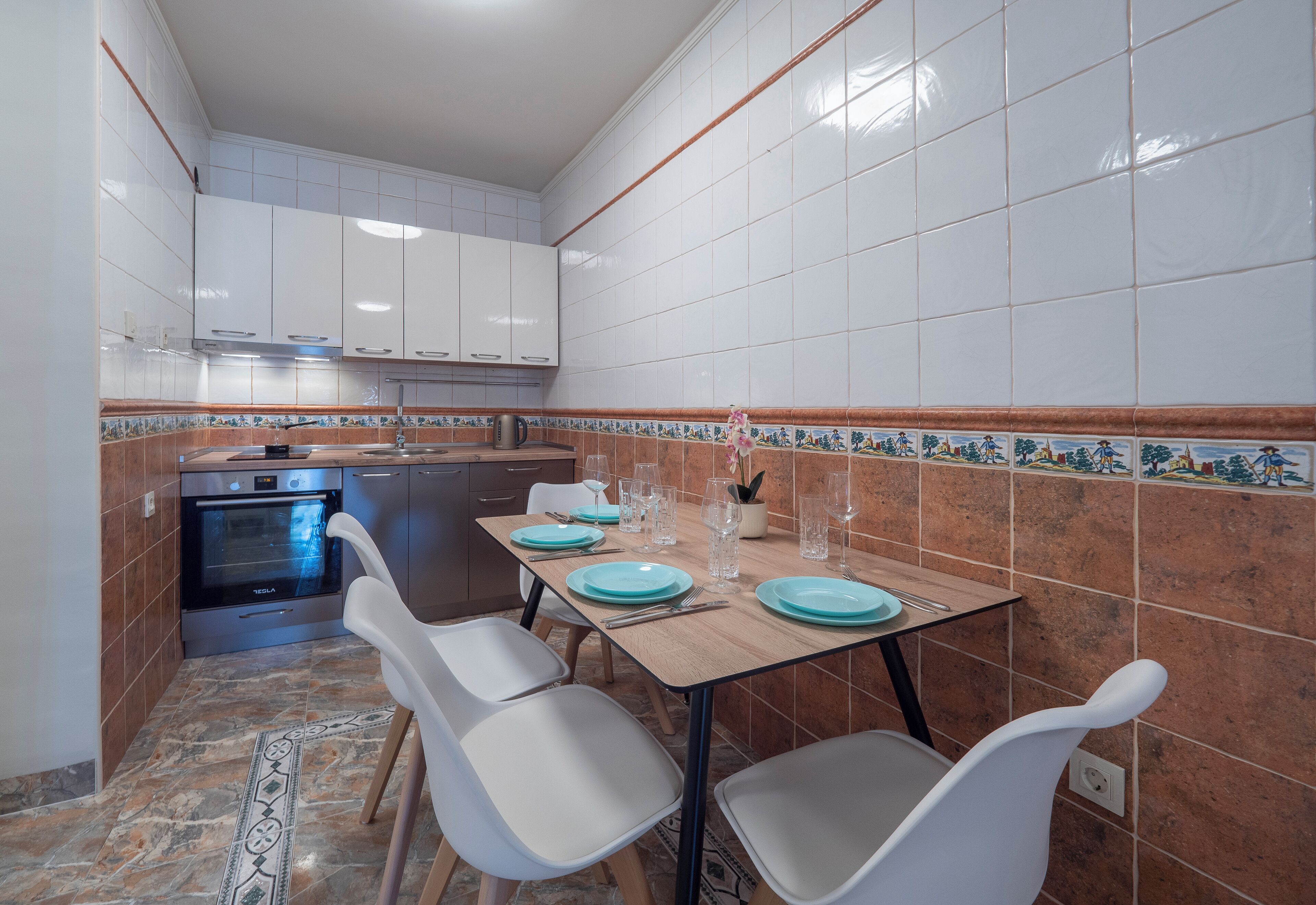 A compact kitchen with white cabinets, a built-in oven, and a dining area with a table set for four.